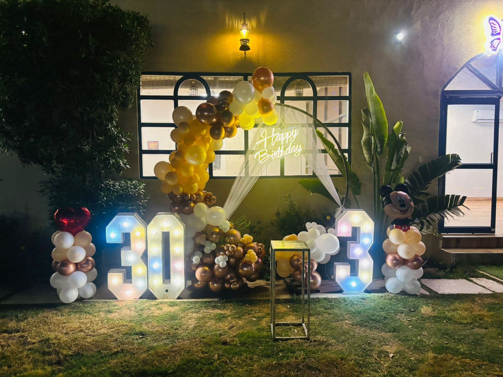 Outdoor garden birthday setup with warm lighting and lit number marquees